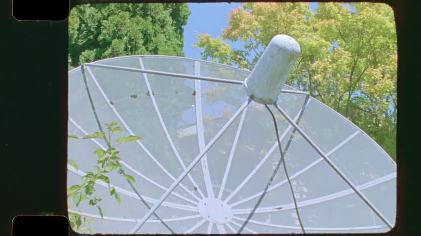 Vintage film captures an old-fashioned mesh satellite dish in a backyard garden on a sunny day