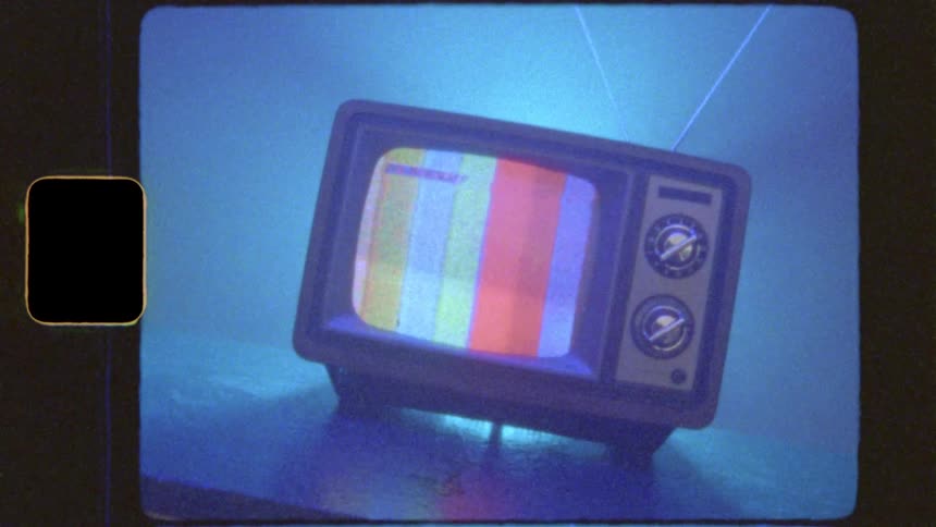 Super 8mm style footage shows a vintage TV with color bars as the background light pulses through a spectrum of colors