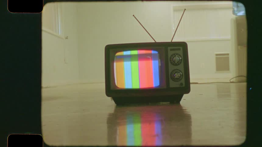 A vintage television displays color bars on its screen while sitting on the floor of an empty room, captured on authentic film