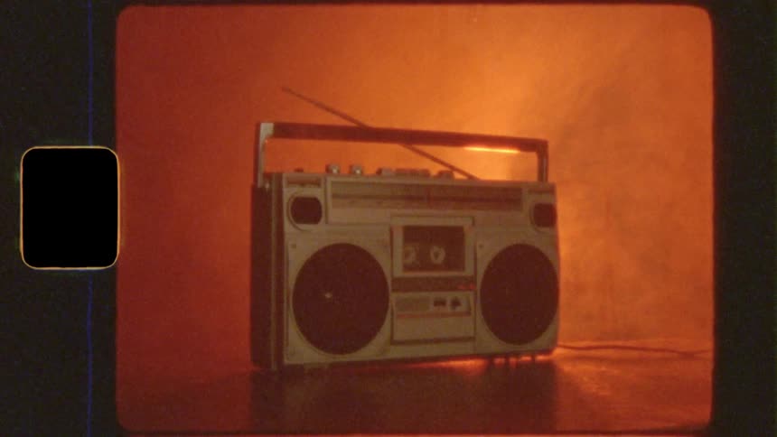A vintage 80s boombox sits on a table in a smoky room with flashing colorful lights and a retro film effect