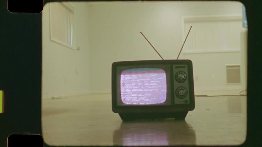 Super 8mm film captures a vintage television displaying static on the reflective floor of an empty, stark room