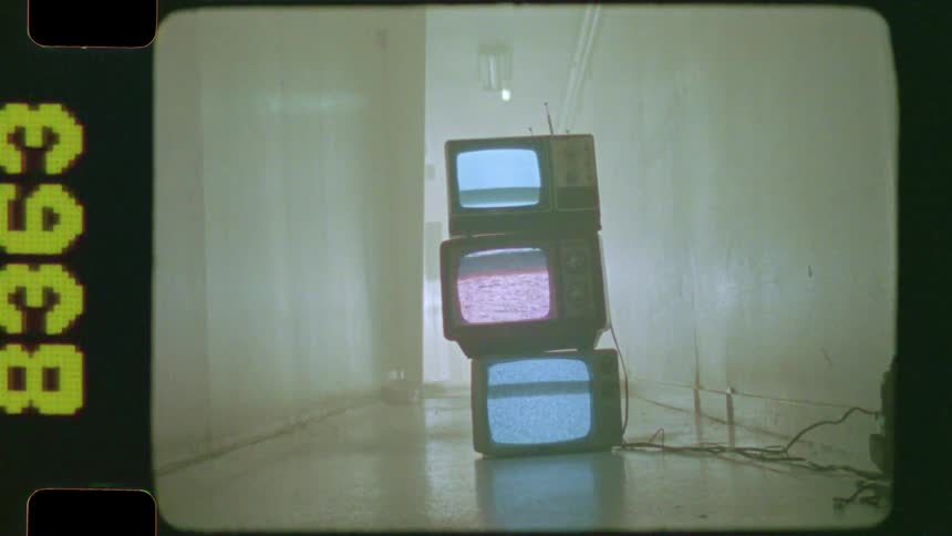 Three stacked retro televisions with flickering static screens sit in a spooky, empty hallway in this authentic vintage film clip