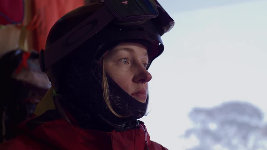 A focused female ski patrol member in her gear studies a mountain map inside a ski hut