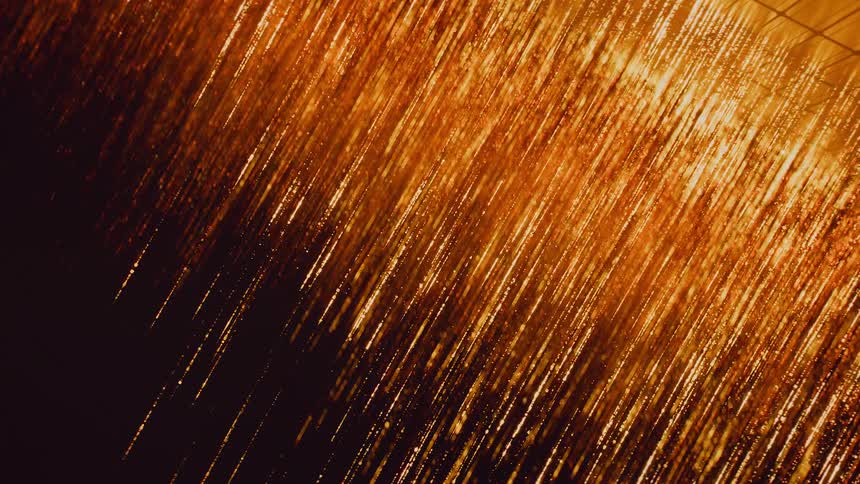 An abstract animation shows streams of shimmering golden particles cascading diagonally against a dark background