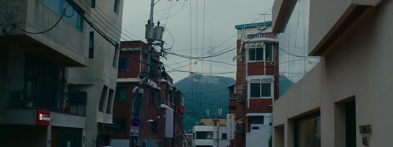 A quiet urban street in Seoul, South Korea, with tangled power lines framing the N Seoul Tower on a distant, hazy mountain
