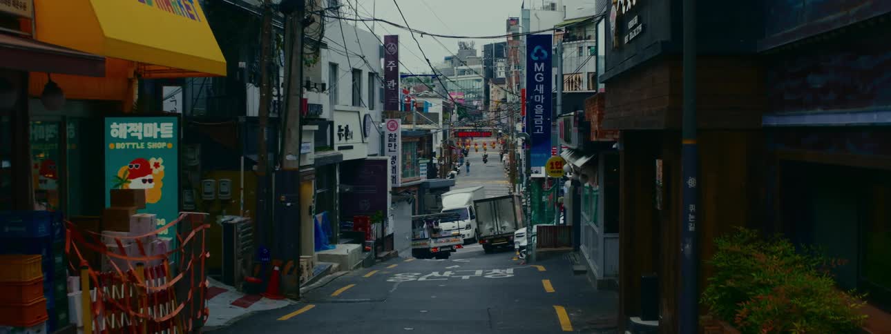A static shot looking down a quiet, hilly urban street in Seoul, South Korea, as a delivery truck backs into a parking spot