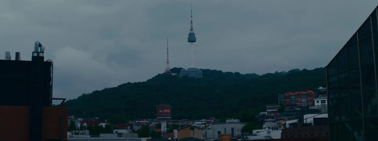 A static wide shot of the iconic Namsan Tower overlooking the city of Seoul on a dark and cloudy day