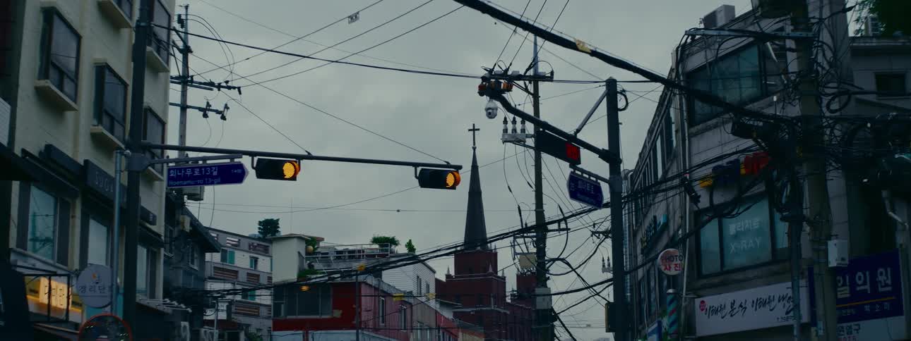 A church steeple rises above a tangled web of power lines and a flashing traffic light on a moody, overcast day in Seoul, Korea