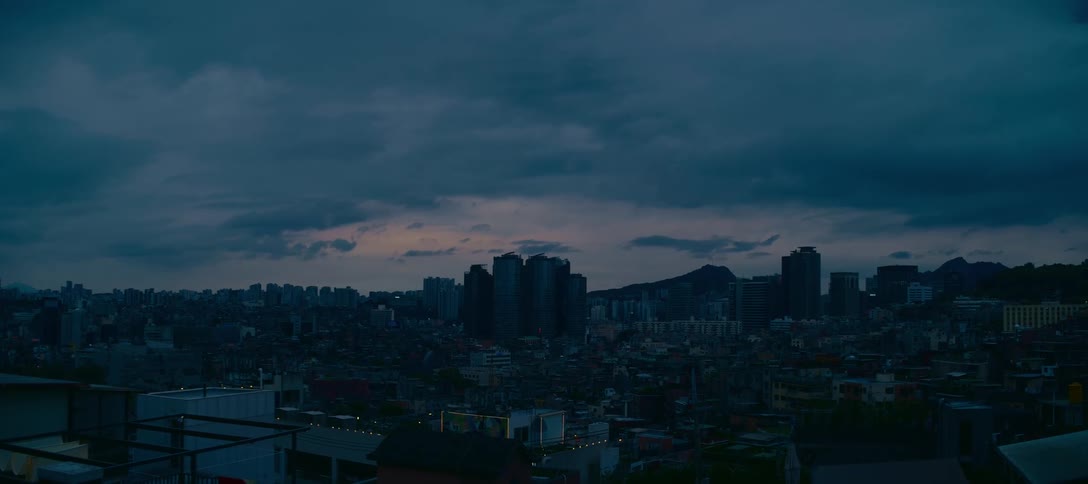 A wide, static view of a sprawling cityscape silhouetted against a dark, moody sky during the quiet moments of twilight