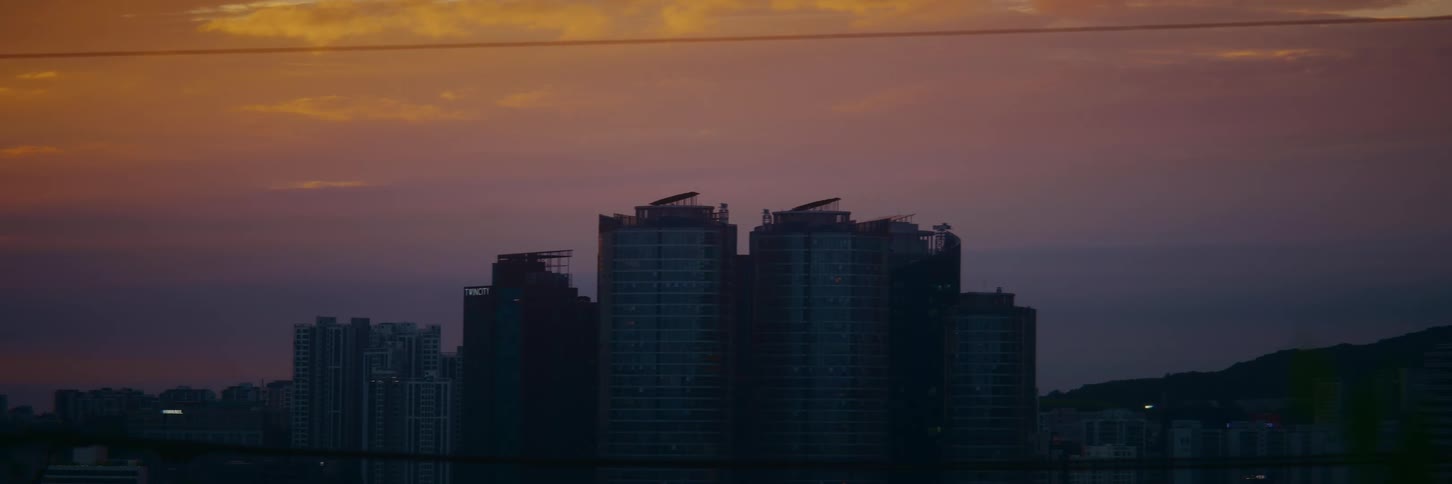 Tall apartment buildings are silhouetted against a beautiful, colorful sky at dusk
