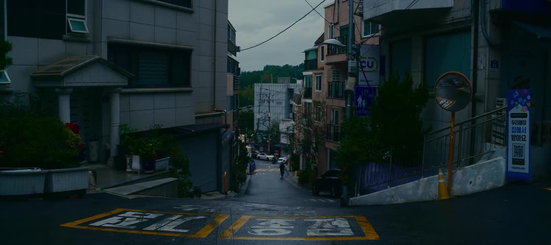 A static wide shot of a quiet, steep residential street in a Korean city on a gloomy, overcast day