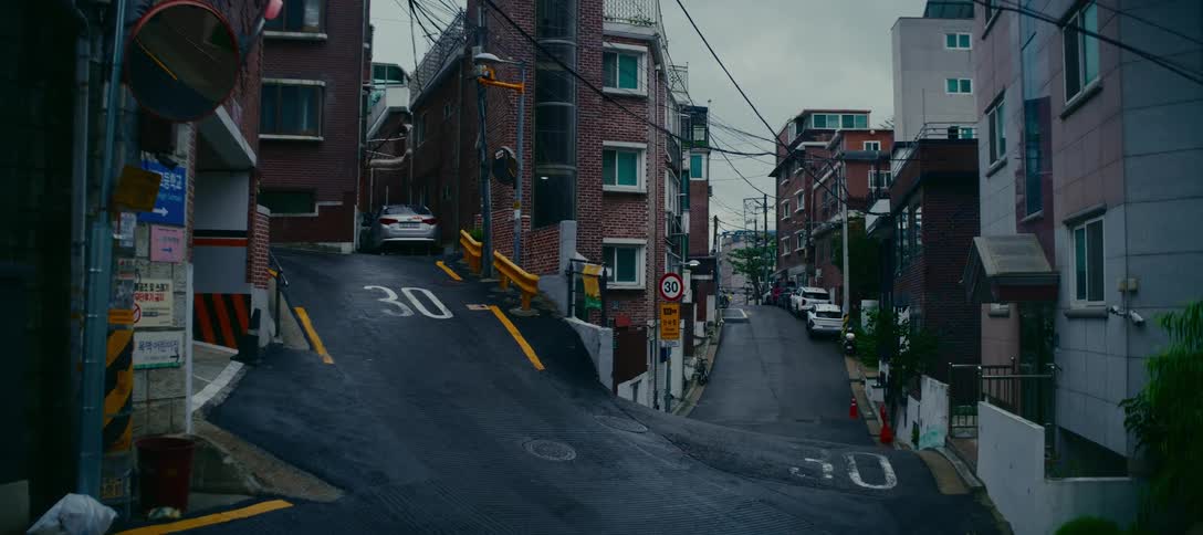 A quiet, hilly street forks in a residential neighborhood of Seoul, South Korea on a wet, overcast day
