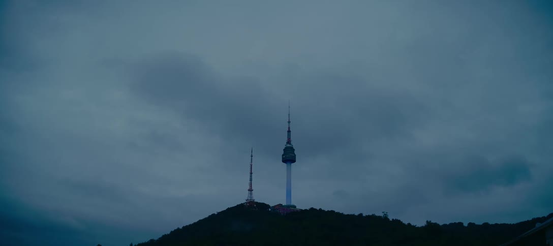The iconic N Seoul Tower stands atop Namsan Mountain against a backdrop of moody, dark clouds at dusk