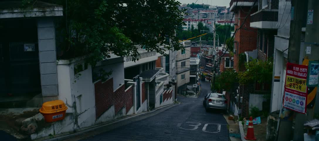 A quiet, steep street winds down through a dense residential neighborhood in Seoul, South Korea