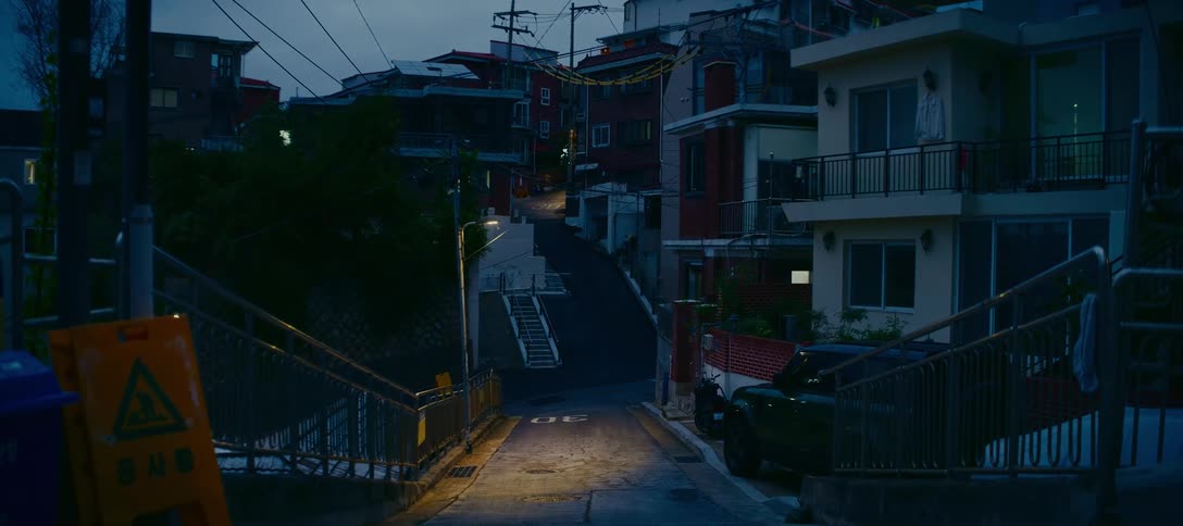 An empty, steep street in a quiet residential neighborhood in Seoul, South Korea is illuminated by a single street lamp at dusk
