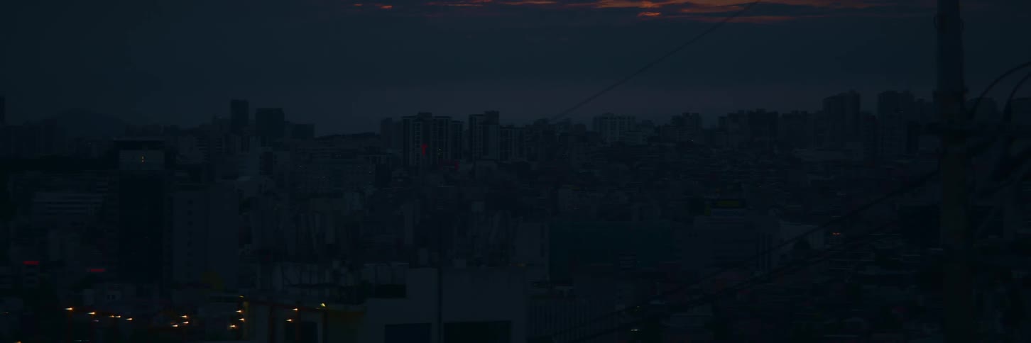 A timelapse of a city skyline transitioning from a fiery sunset at dusk to the twinkling lights of night