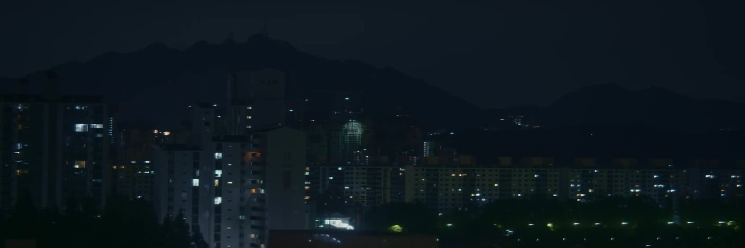 A still shot of city apartment buildings at night with mountains silhouetted in the background