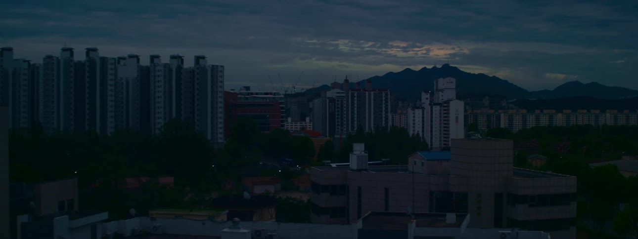 A still shot of a city skyline with apartment buildings and a distant mountain range at twilight