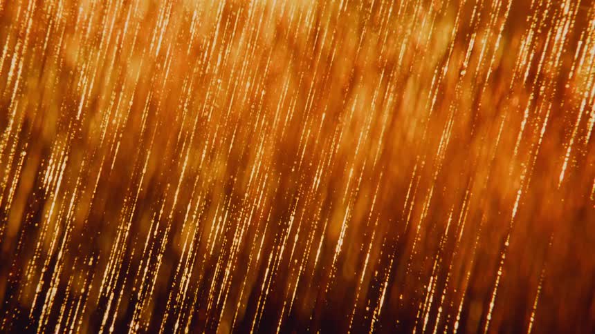 A mesmerizing slow motion cascade of shimmering golden particles falls like rain against a warm, abstract background