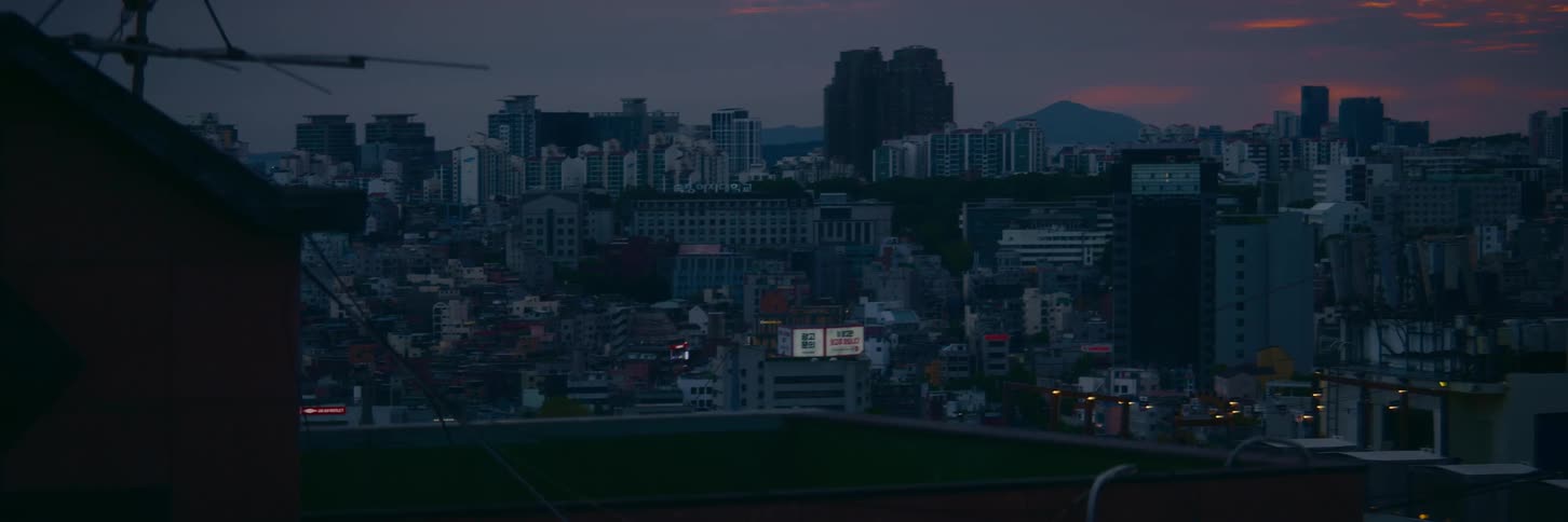 A wide, atmospheric shot of a dense urban cityscape at dusk, with buildings stretching towards distant mountains