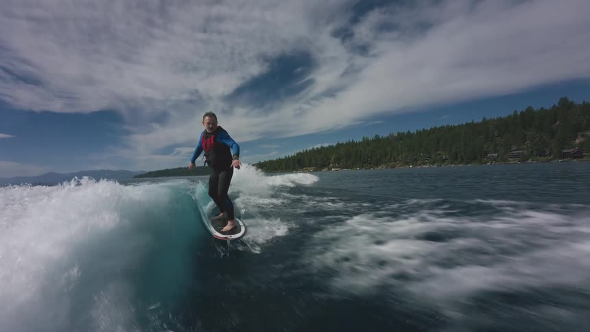 Cinemagraph of a man in a wetsuit wakesurfing on a pristine blue lake on a sunny summer day