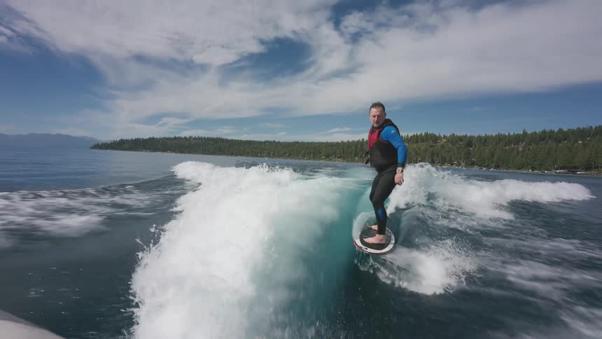 Seamless loop cinemagraph shows a man in a wetsuit skillfully wakesurfing in slow motion on a beautiful lake