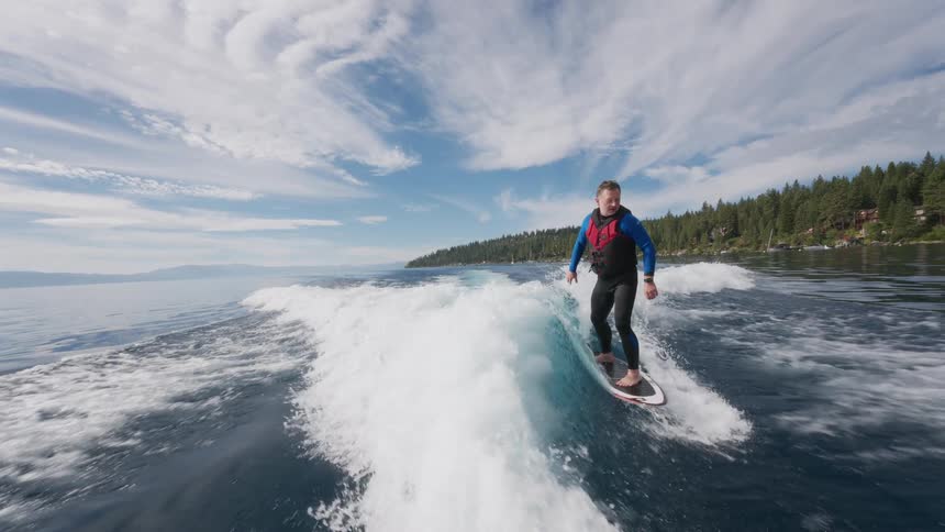 Cinemagraph of a man in a wetsuit wakesurfing in slow motion on a beautiful mountain lake