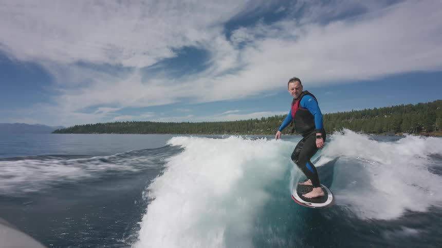 Slow motion cinemagraph of a smiling man in a wetsuit wake surfing on a beautiful clear lake