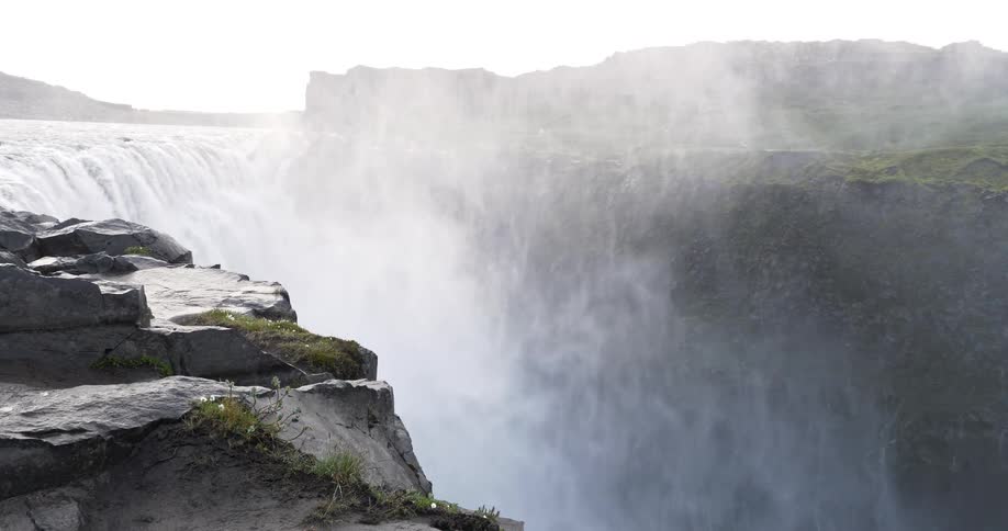 A powerful waterfall crashes into a deep canyon, kicking up a thick cloud of mist from a rocky viewpoint