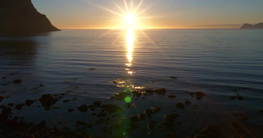 Slow camera tilt reveals a stunning sunrise reflecting over a calm sea from a rocky shore