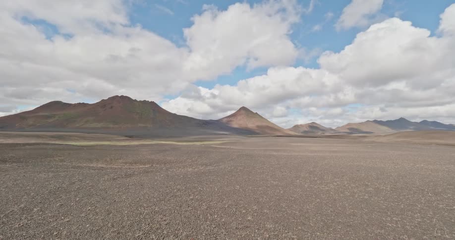 Time-lapse of clouds and their shadows moving across a vast, barren volcanic landscape with distant mountains