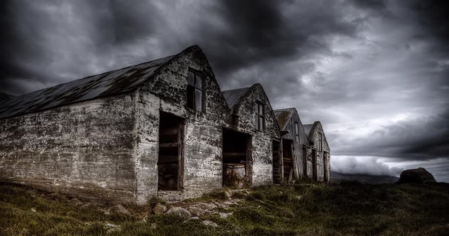 A dramatic HDR time-lapse shows dark storm clouds passing over a row of desolate, abandoned buildings
