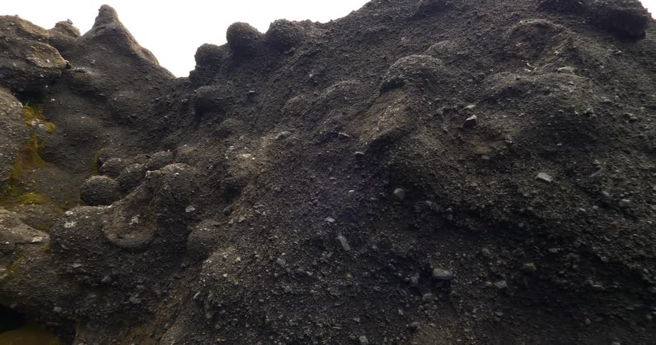 Slow dolly shot revealing the intricate texture of dark, bulbous volcanic rock formations against a white sky