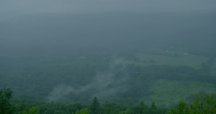 A wispy clouds moves over a forested landscape