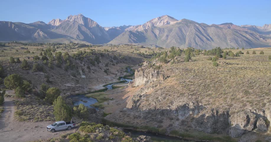 A majestic aerial view of the Eastern Sierra mountains with a creek winding through a vast valley as the camera slowly pulls back