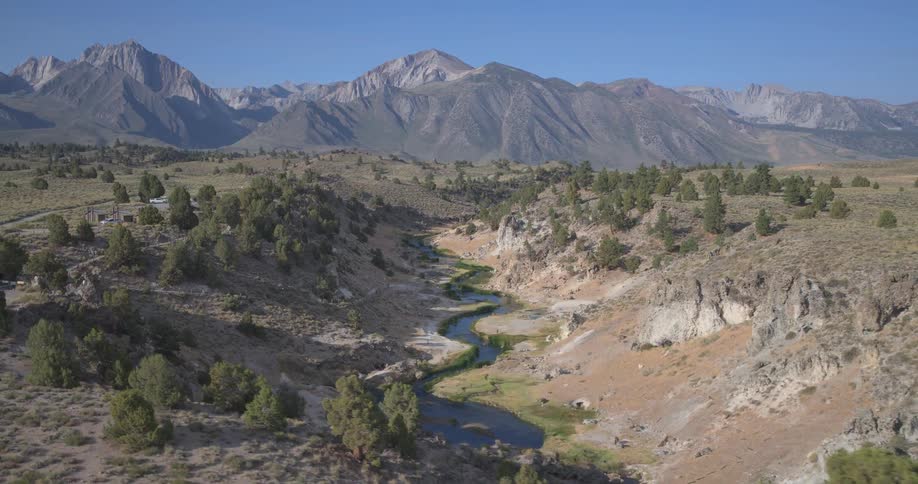 A stunning aerial view pulls back to reveal a winding river flowing through a desert canyon with majestic mountains in the distance