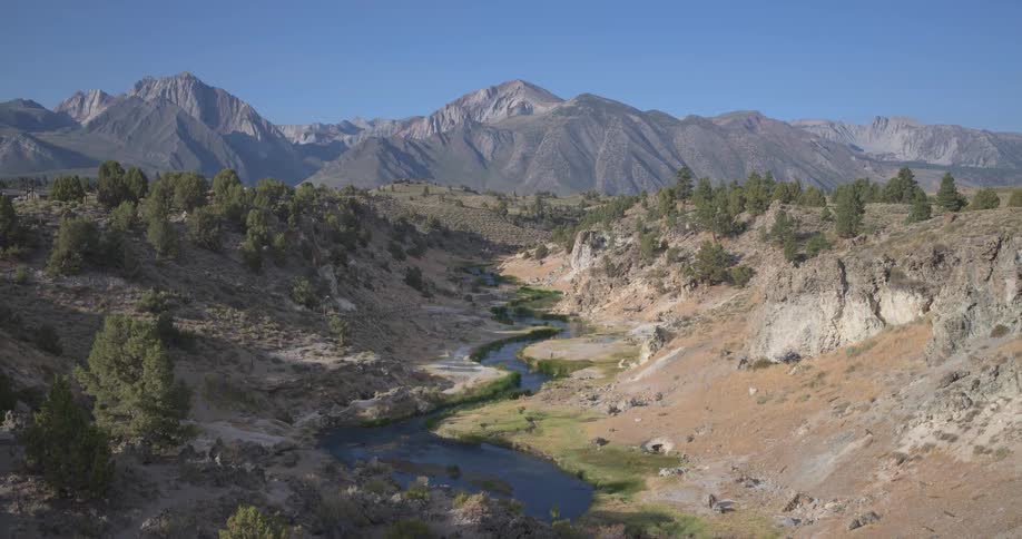 A hiker with a backpack gazes out at a picturesque winding river flowing through a valley with majestic mountains in the background