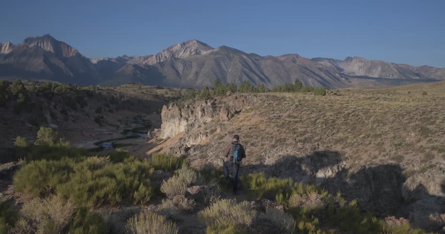 A photographer with a backpack hikes away from his truck along a canyon rim to capture the stunning mountain landscape at golden hour