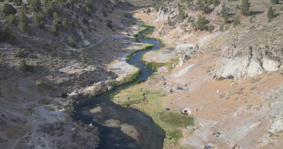 A slow pullback from a winding river reveals the expansive Hot Creek Geological Site and the majestic Sierra Nevada mountains in the background