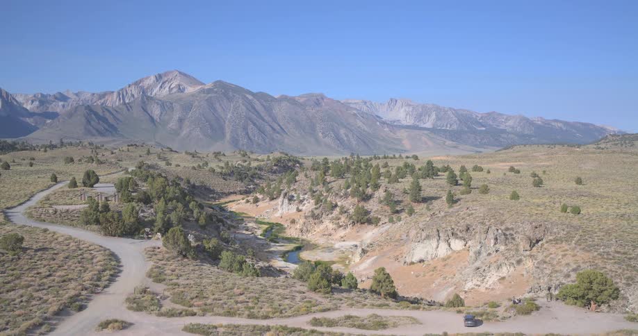 Aerial drone slowly pushes forward over a high desert valley to reveal a meandering creek with the Eastern Sierra Nevada mountains in the background