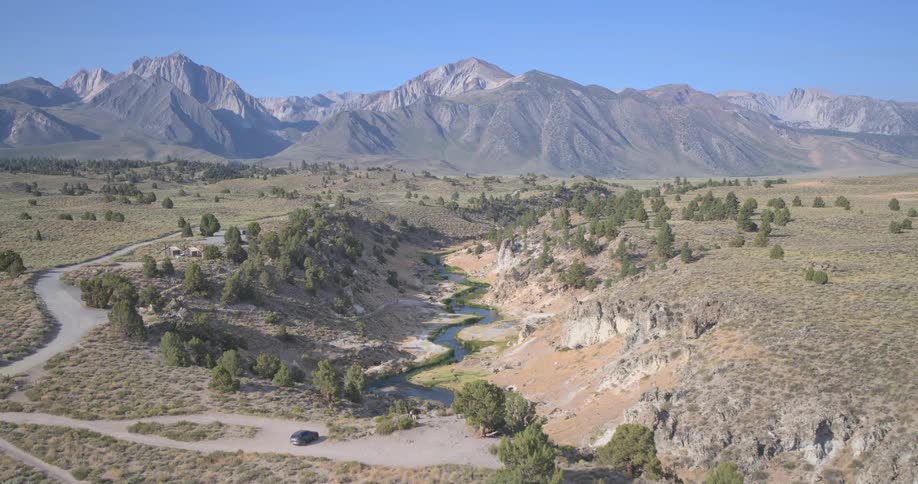 An expansive aerial shot slowly pulls back to reveal a winding creek through a desert canyon against the backdrop of the Sierra Nevada mountains