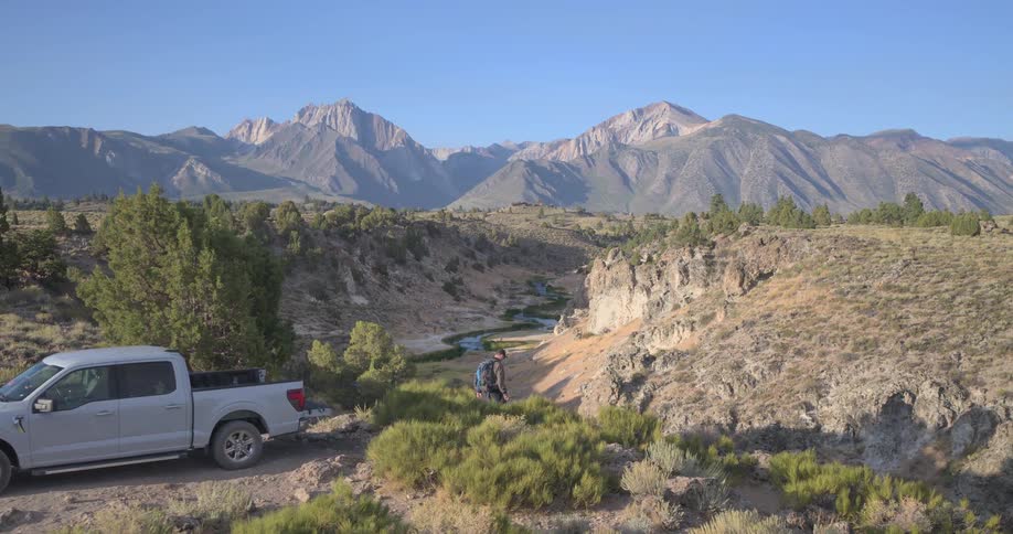 A man on a road trip parks his pickup truck and walks to a scenic overlook to photograph the magnificent mountain and river valley below
