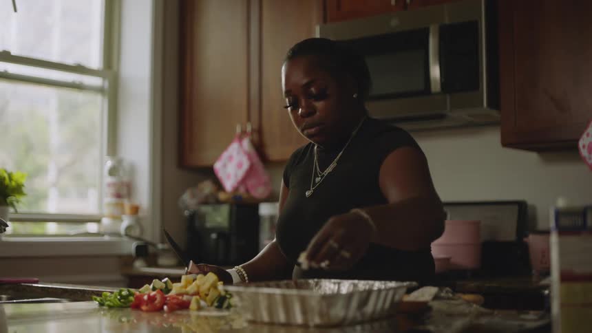 An African American woman prepares a meal in slow motion, mixing vegetables and ingredients in a foil pan in her kitchen
