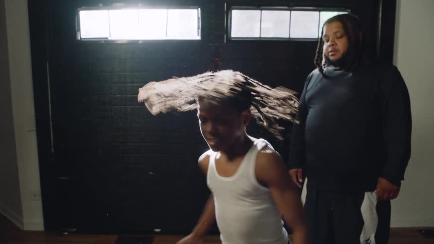 A father watches his son dance with intense passion and energy in a dimly lit room, captured in dramatic slow motion