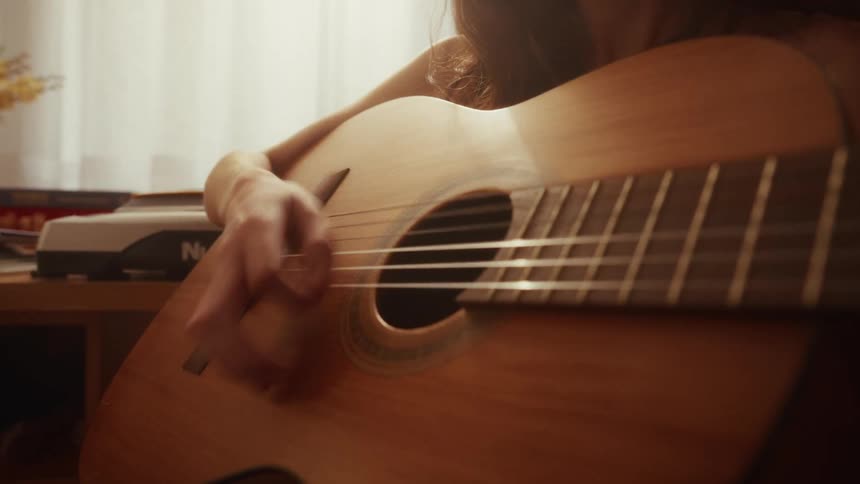 A young woman passionately plays a classical acoustic guitar indoors with soft sunlight filtering through the window