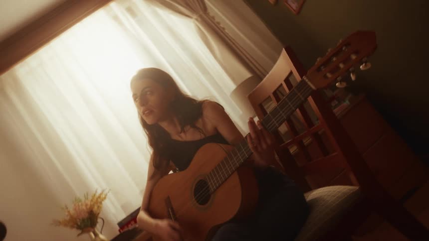 A talented young woman passionately sings while playing the acoustic guitar in her cozy, sunlit room