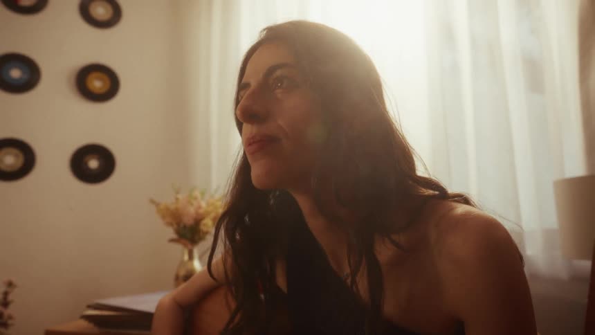An artistic young woman plays her acoustic guitar in a sunlit room, smiling serenely as she connects with her music