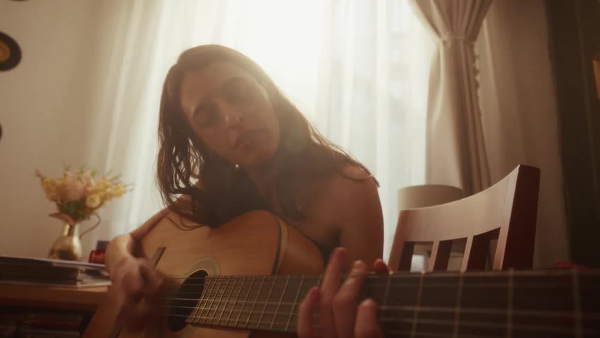 A soulful young woman plays a heartfelt melody on her acoustic guitar in a warmly lit room