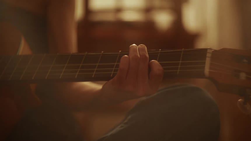 Close-up of a musician's fingers pressing down on the fretboard of a classical guitar