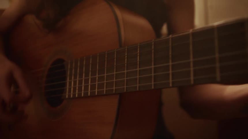 An intimate close-up shot of a musician's hands skillfully playing chords and strumming an acoustic guitar in a warm, dimly lit room